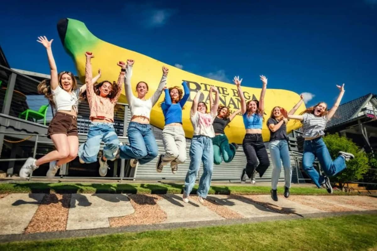 A group of people jumping in unison in front of a large banana statue on a sunny day.