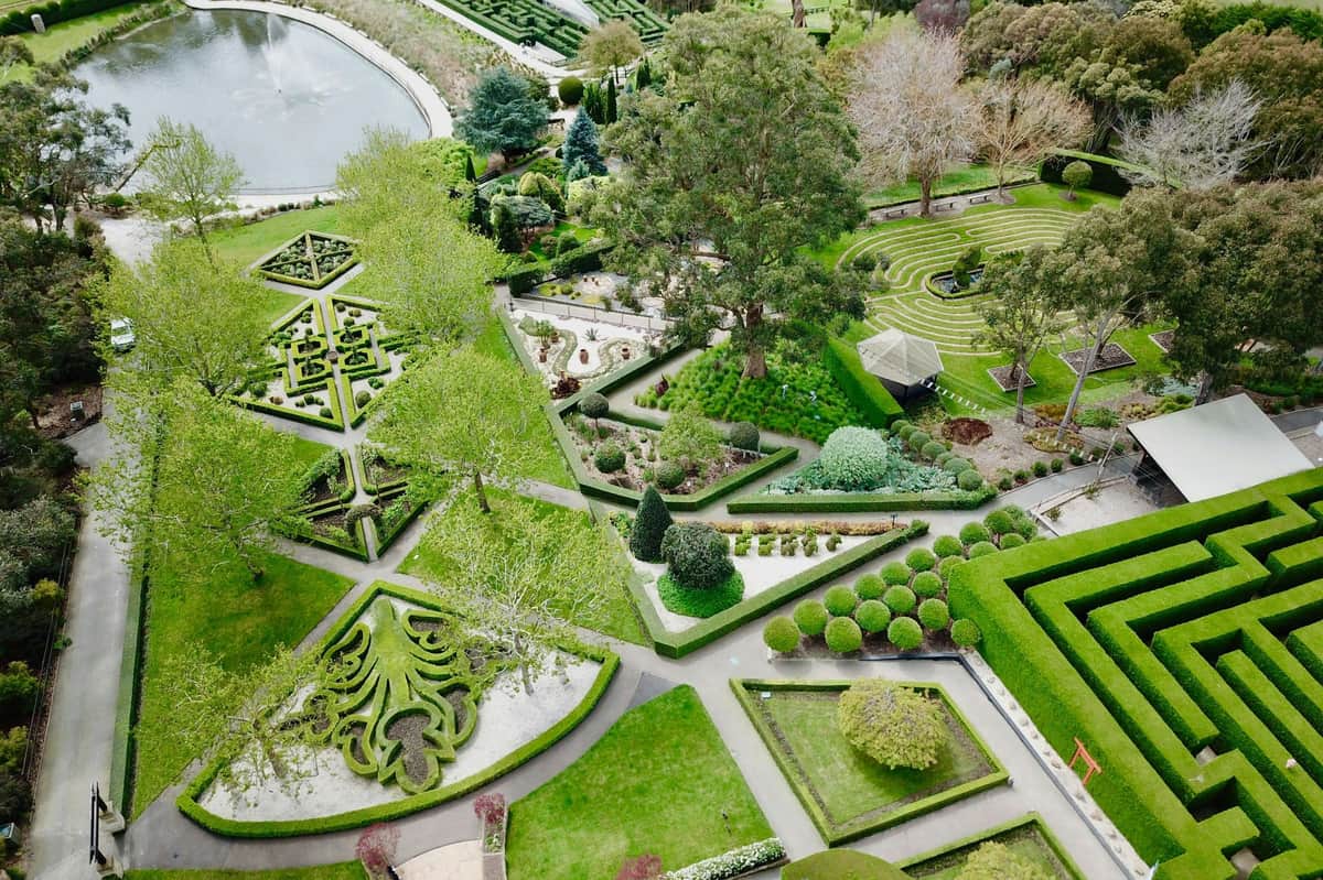 Vue aérienne d'un jardin à la française, avec des haies aux motifs géométriques, des allées, des arbres et un petit étang à l'arrière-plan.