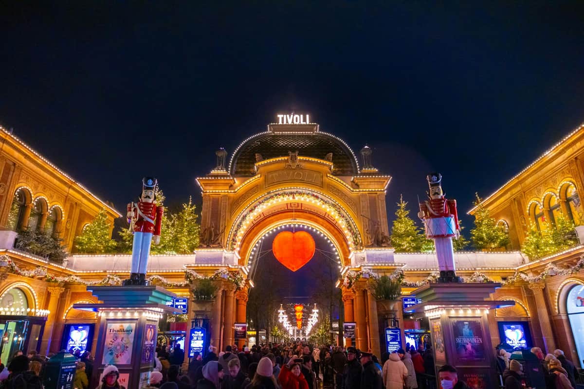People gather under Tivoli's illuminated archway adorned with festive lights, large nutcracker statues, and a glowing red heart.