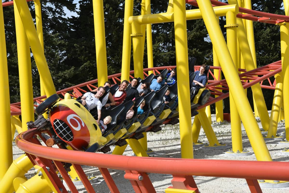 People riding a yellow and red rollercoaster with loops and turns, surrounded by trees.