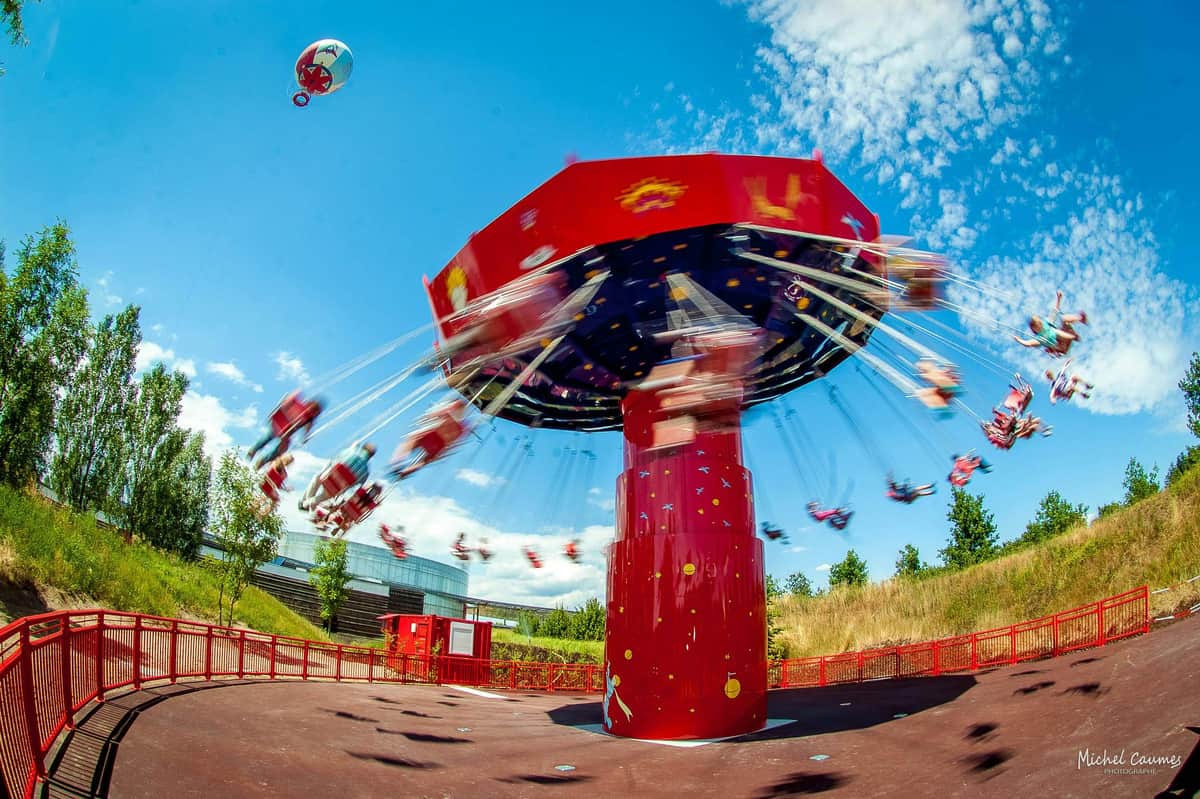 A red swing carousel in motion against a blue sky with people seated and a balloon floating nearby.