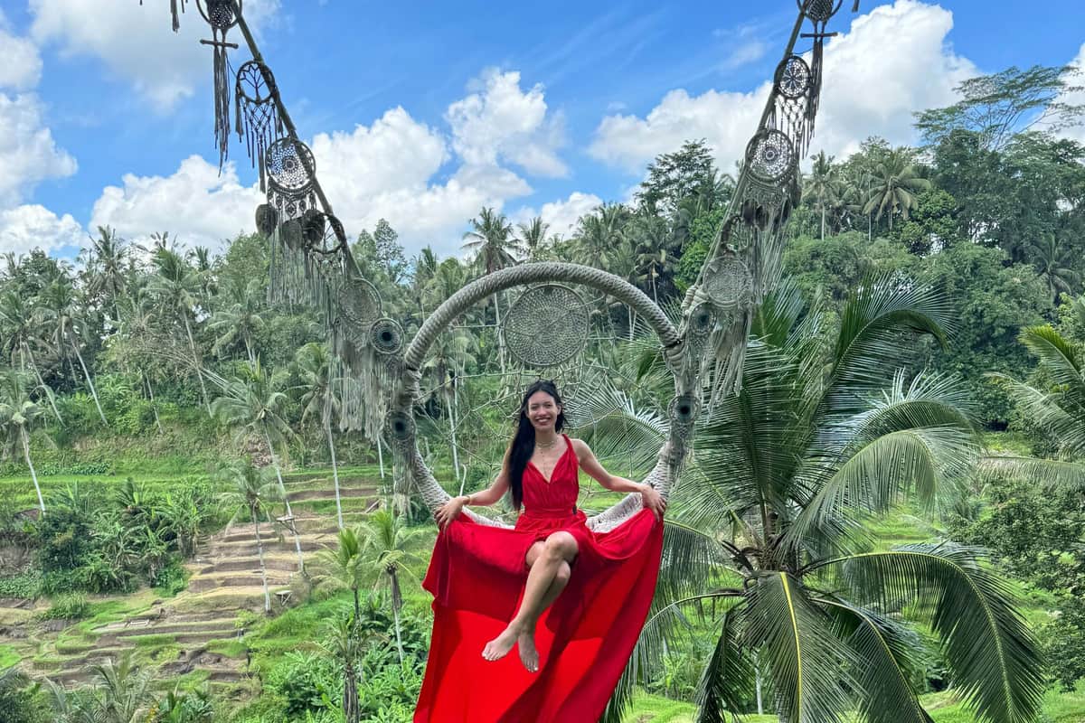 A woman in a red long dress swinging in the Dreamcatcher Swing above the beautiful green rice terraces at U Fun Field Park