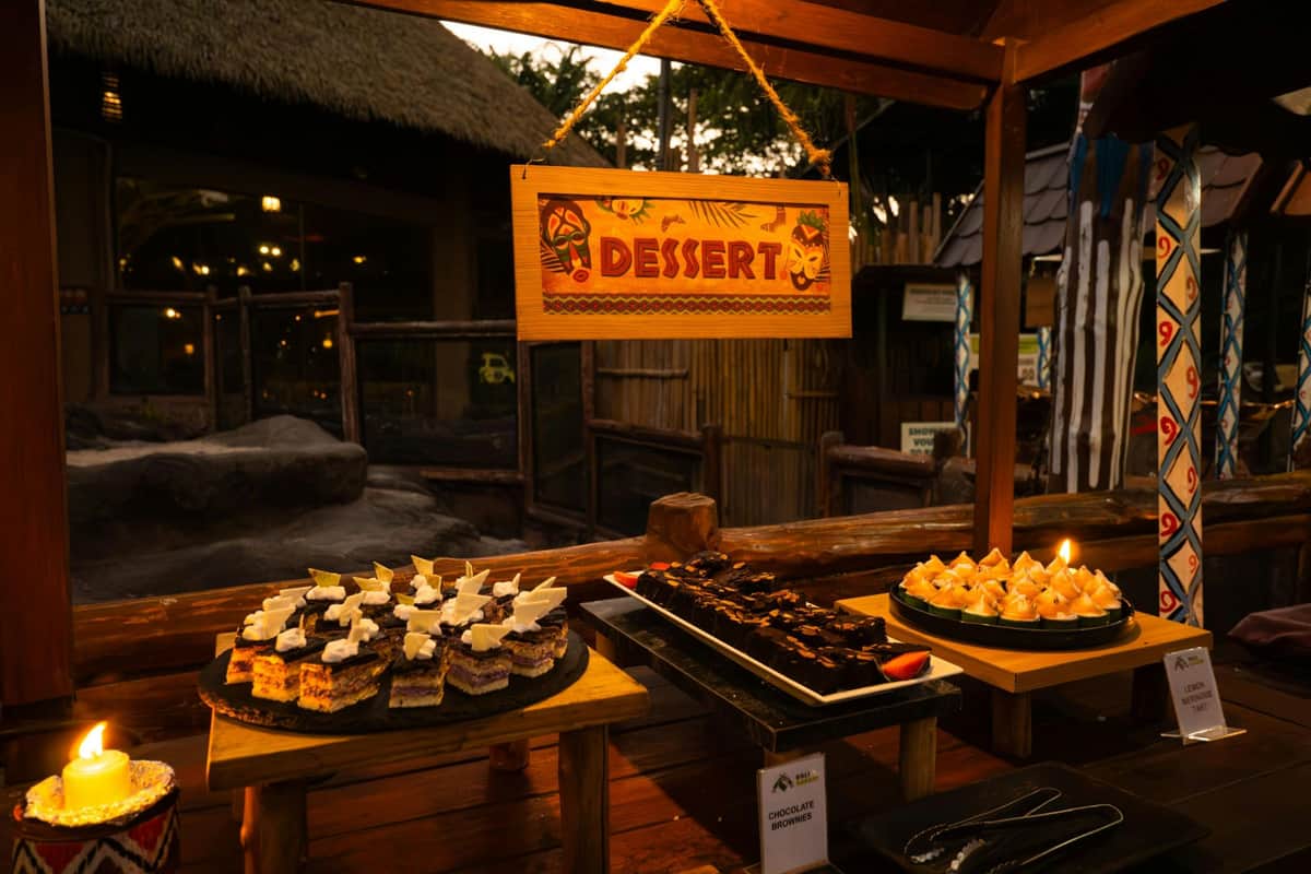A dessert buffet with various cakes and pastries displayed on plates under a sign that reads 'Dessert' in warm lighting.