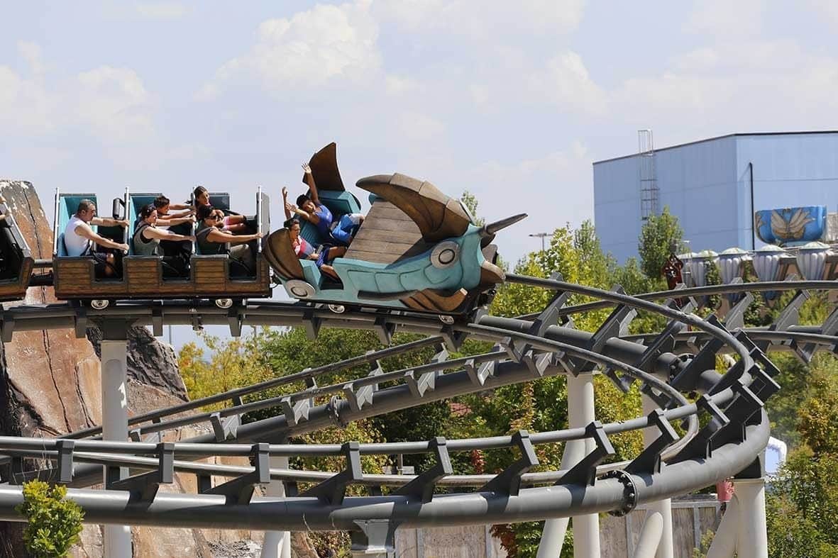 People riding a detailed, dragon-themed rollercoaster on a sunny day with trees and a building in the background.