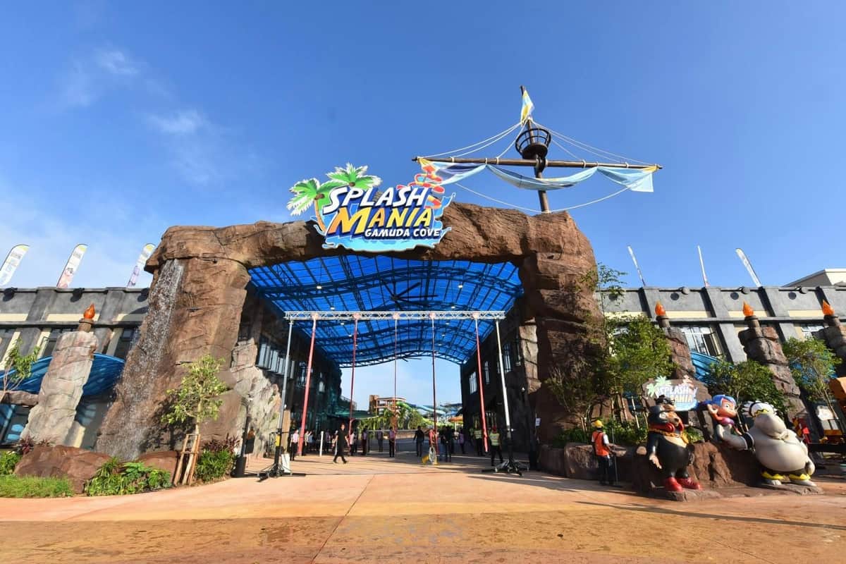 Entrance to "Splash Mania" water park with a blue roof structure, rock archway, and playful pirate-themed decorations.
