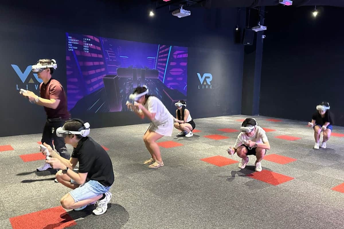 VAR LIVE VR Theme Park Kuala Lumpur: wstęp do MyTOWN Cztery osoby noszące gogle i kontrolery VR angażują się w wirtualną grę w pokoju z wystrojem o tematyce VR.