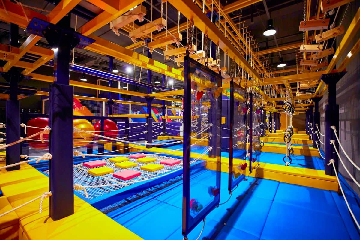Circuito de cuerdas y obstáculos en interior con estructuras amarillas y azules, que incluye paredes de escalada, redes y plataformas de equilibrio.