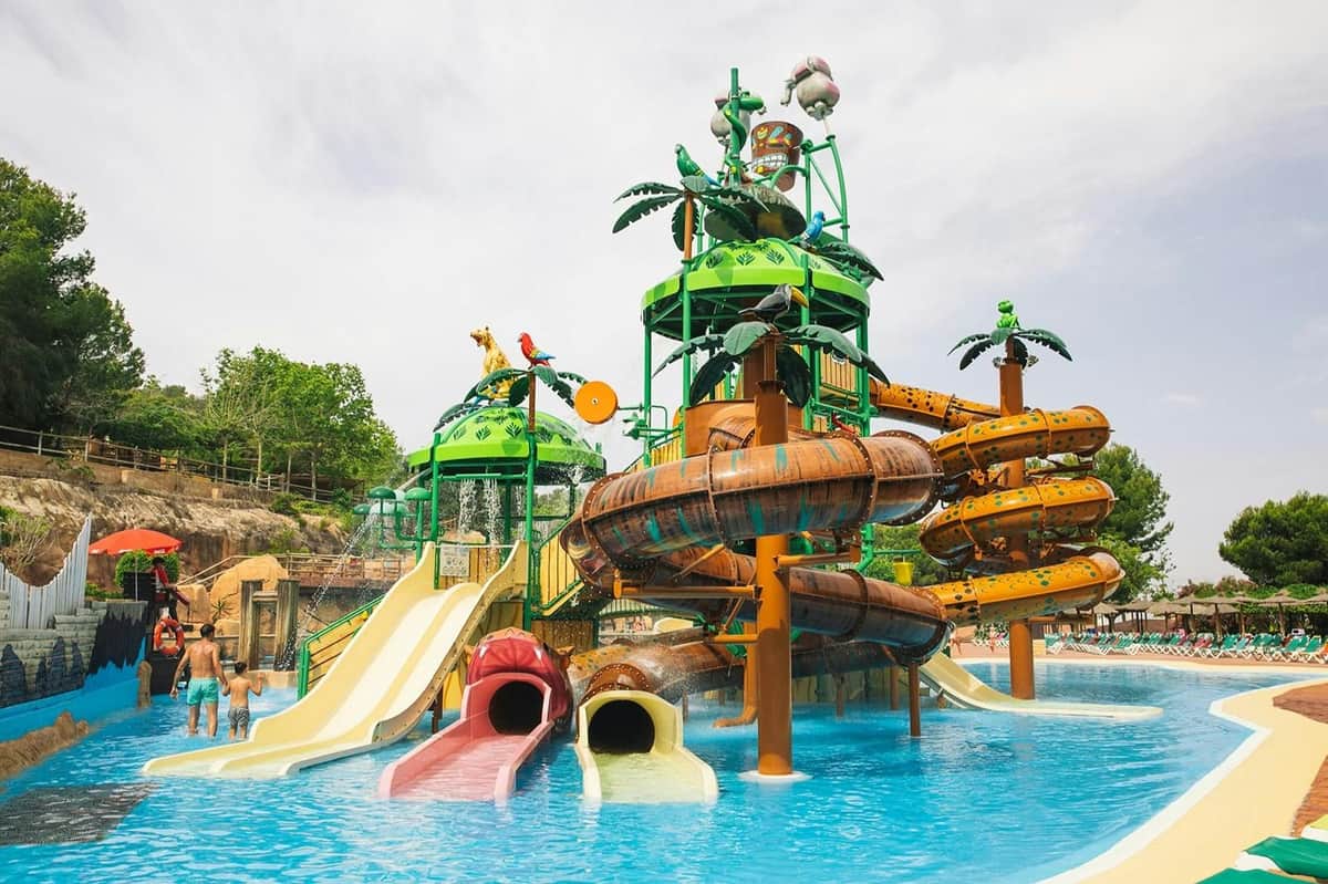 Colorful water park with slides, tubes, and water play structures surrounded by a pool and tropical-themed decorations.