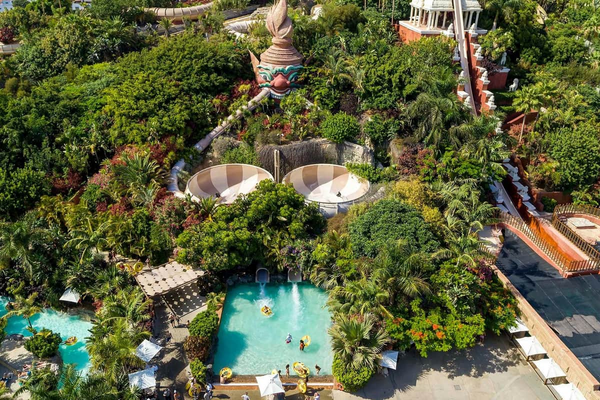 Aerial view of a water park with slides, pool, greenery, and people enjoying various recreational activities.