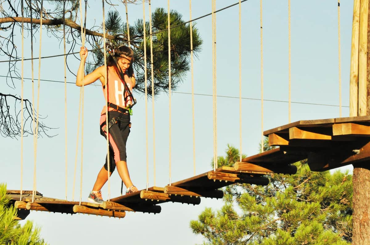 Tirolinas Go Mallorca: Adventure Park A woman crosses a suspended rope bridge in an adventure park, surrounded by trees and secured with a harness.