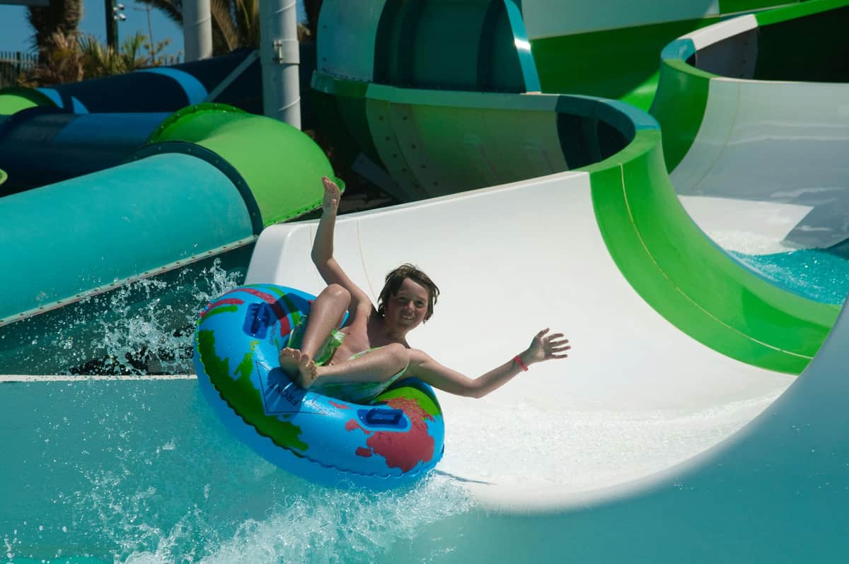 Aqualava Water Park: Entry Ticket A person sliding down a water slide on a colorful inflatable tube, with a joyful expression and raised arms.