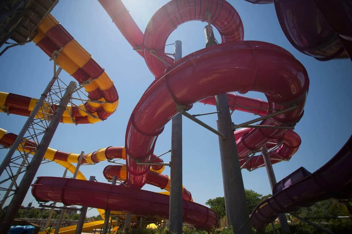 Curving water slides in vibrant red and yellow colors against a blue sky, supported by tall metal pillars.