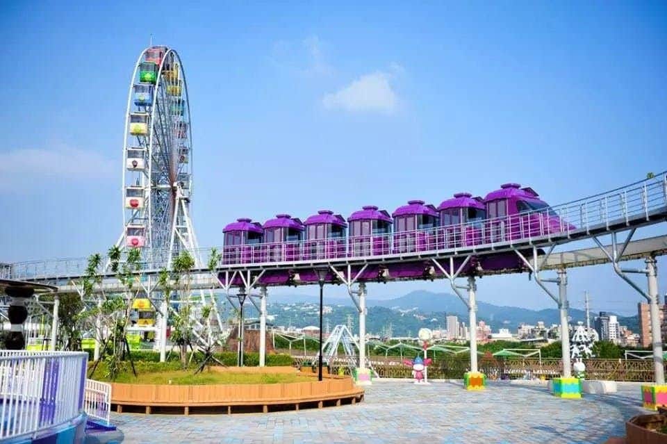 A colorful children's train ride with a ferris wheel and booth in the background under a clear blue sky.