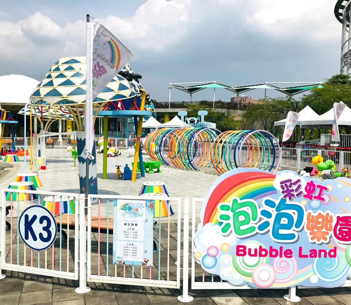 A colorful toy train ride for children passing by a ferris wheel and a concession stand in a sunny amusement park.