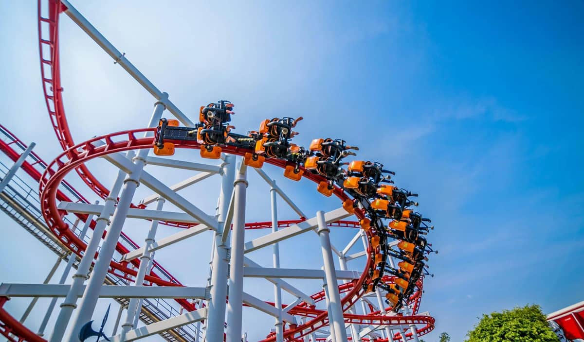 A rollercoaster with orange cars and people riding on red tracks against a clear blue sky.