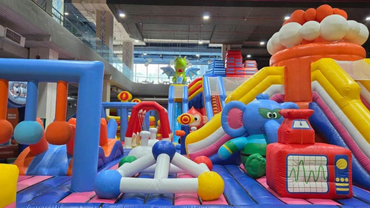 Indoor inflatable play area with colorful slides, tunnels, and animal-themed bouncers under a high ceiling.