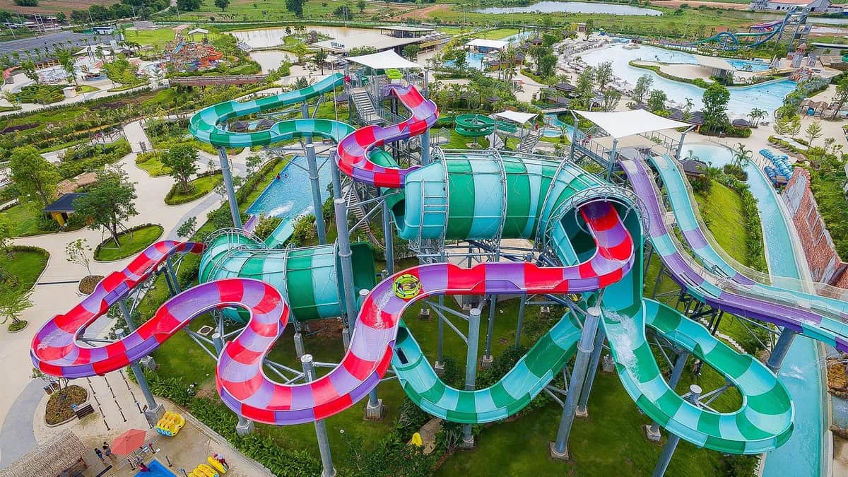 Ramayana Water Park: Skip The Line Ticket An aerial view of a colorful, winding water slide complex with multiple enclosed and open sections, surrounded by green landscape.