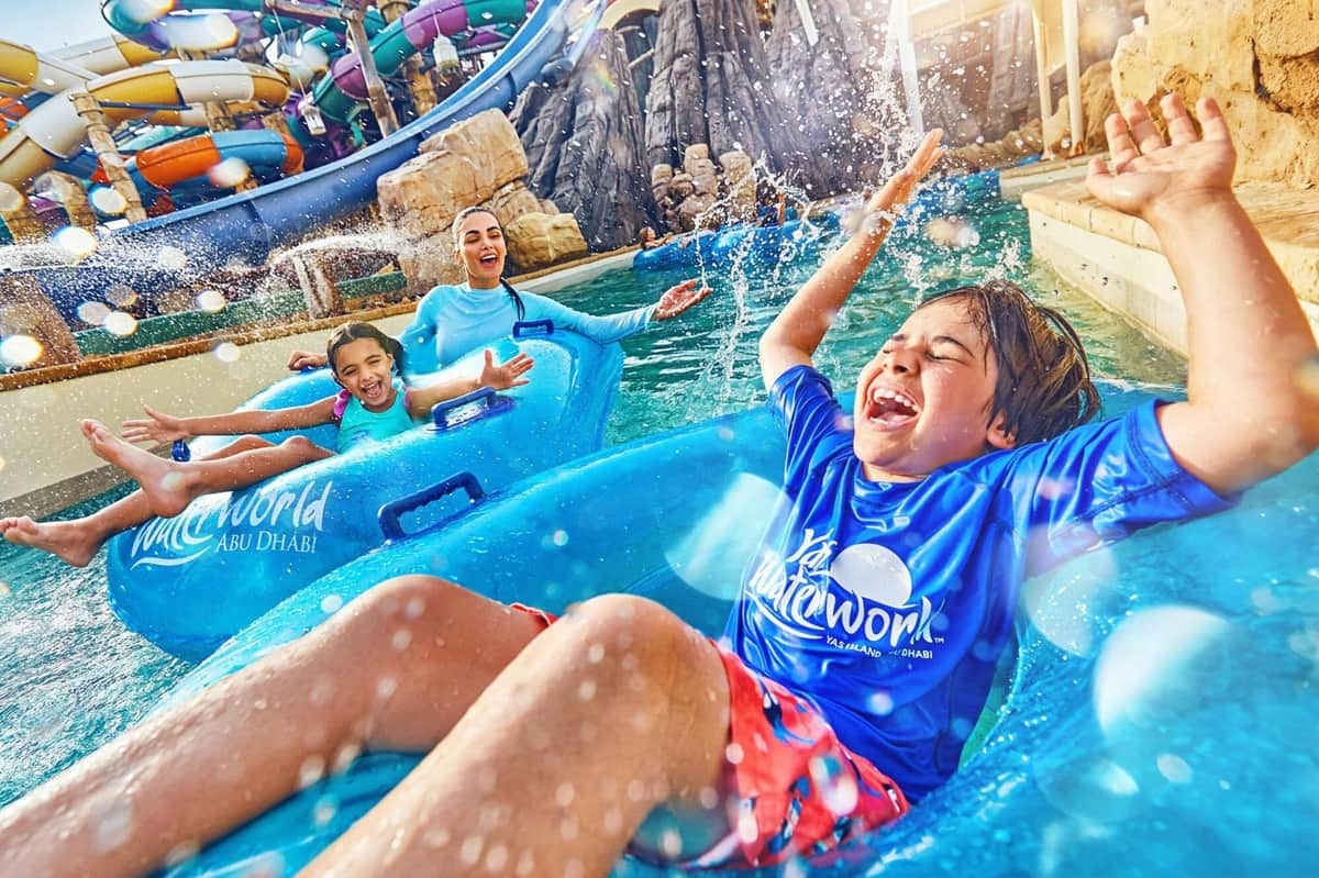 Three people in blue rafts enjoying a water park ride, splashing water around them with joyful expressions.