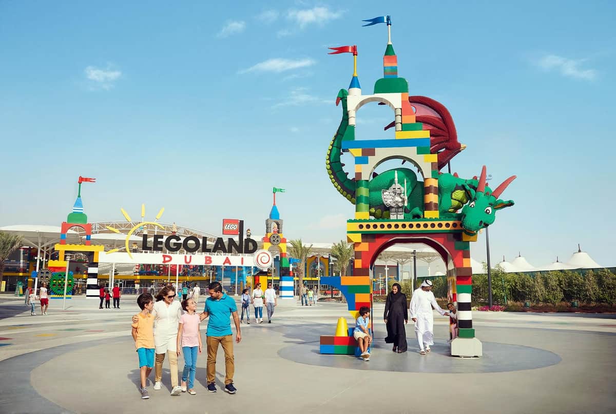 Families walk near the colorful entrance archway adorned with a dragon at LEGOLAND Dubai on a sunny day.