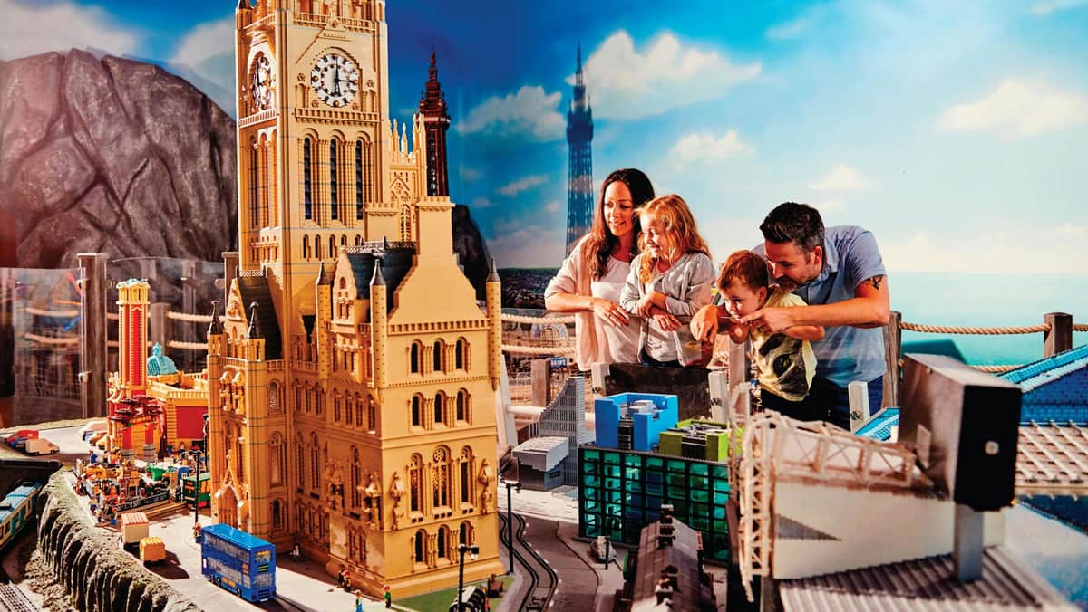 A smiling family of four admires a detailed miniature city display, featuring various buildings and landmarks.