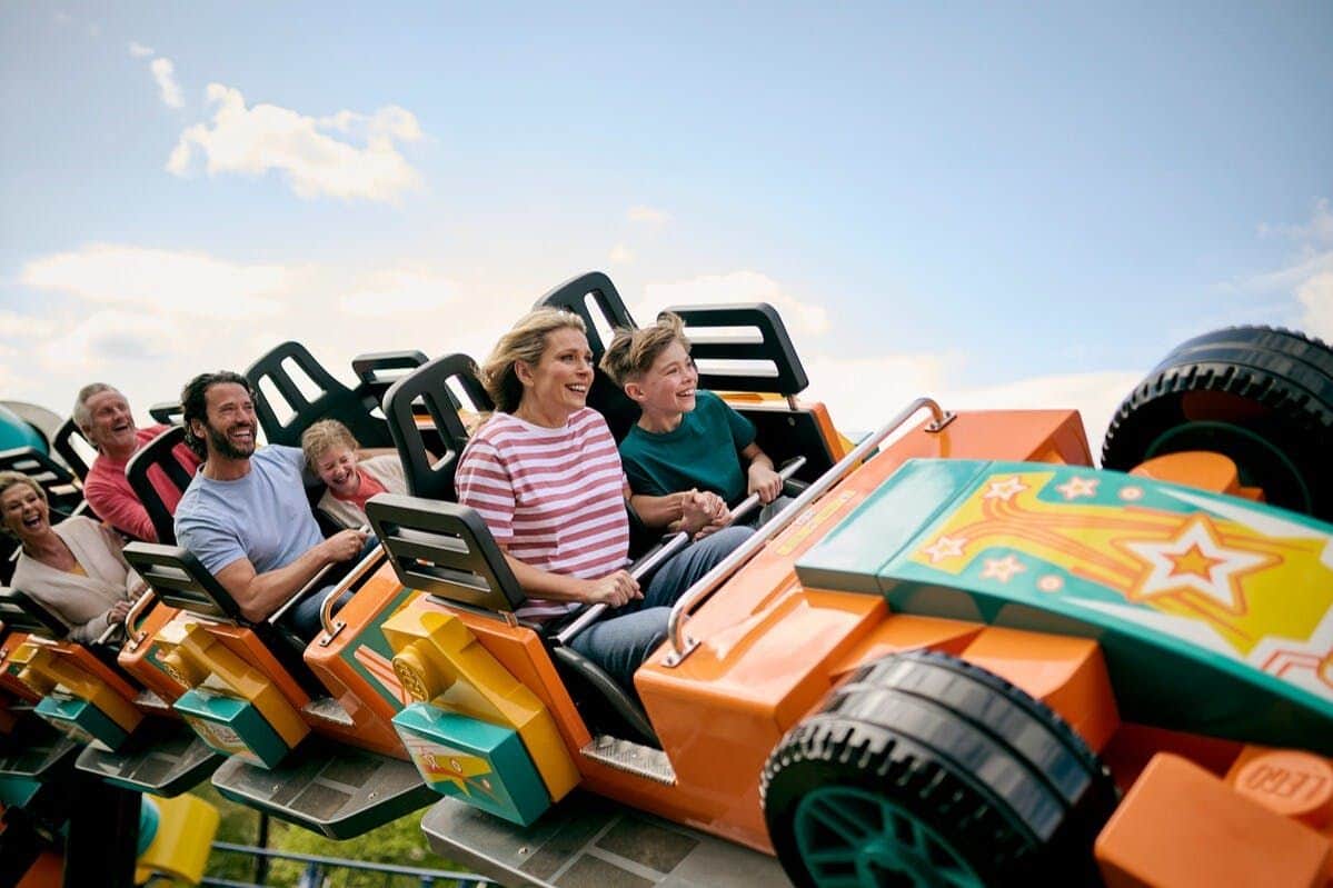 A family enjoys a ride on a colorful roller coaster under a clear blue sky.