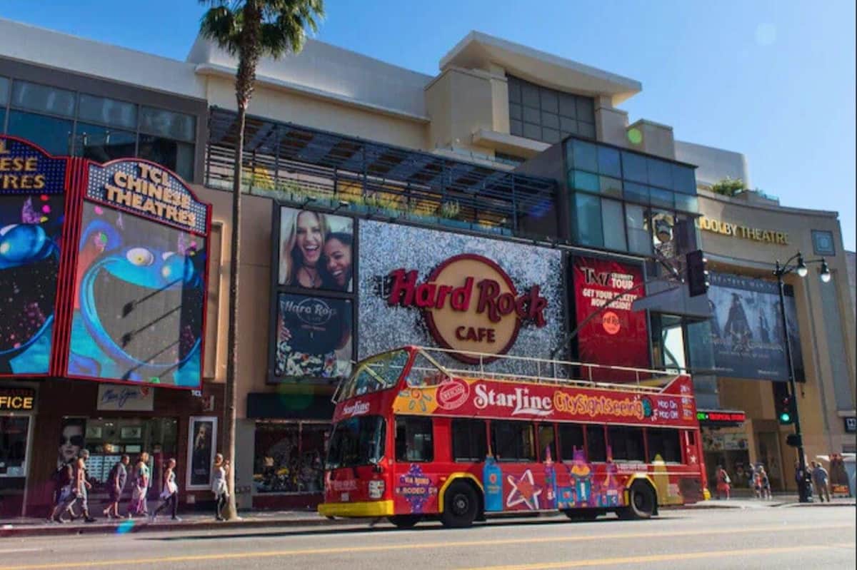 A red sightseeing bus parked in front of the Hard Rock Cafe and TCL Chinese Theatre on a sunny day.