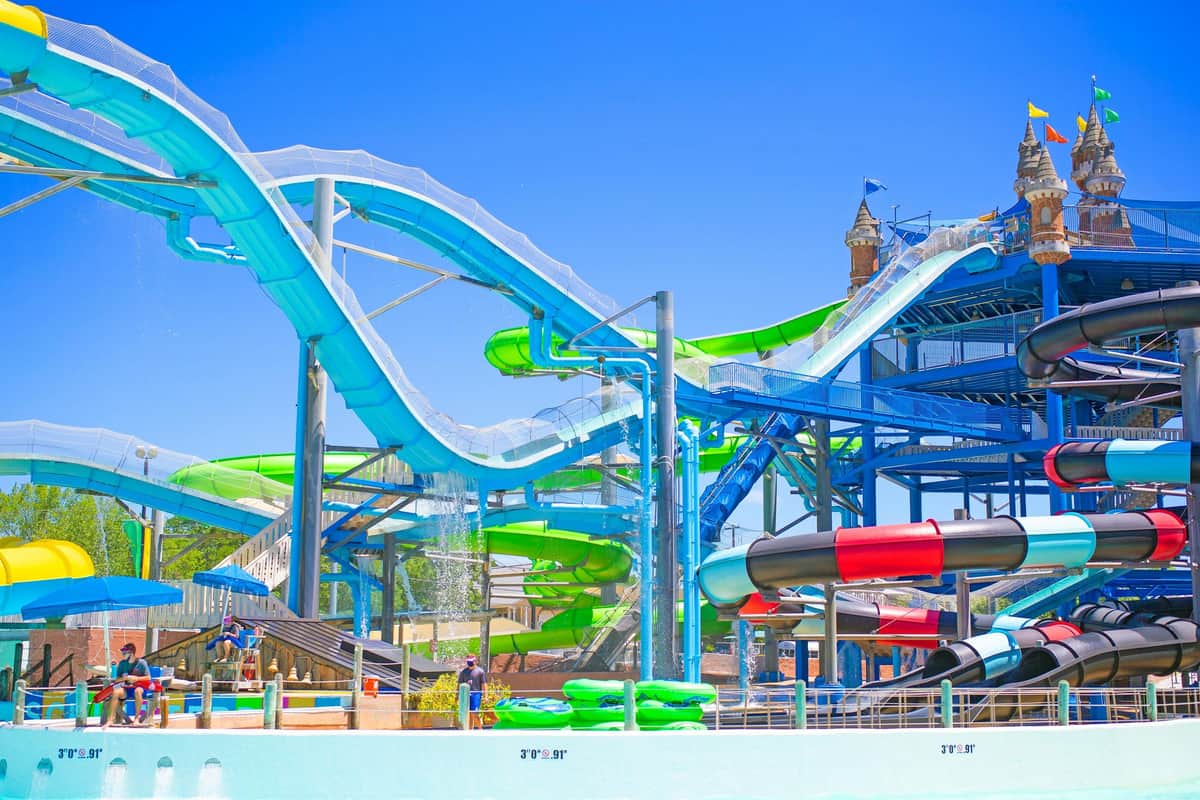 A water park with green water slides, a pirate flag, and a castle-themed structure under a clear blue sky.