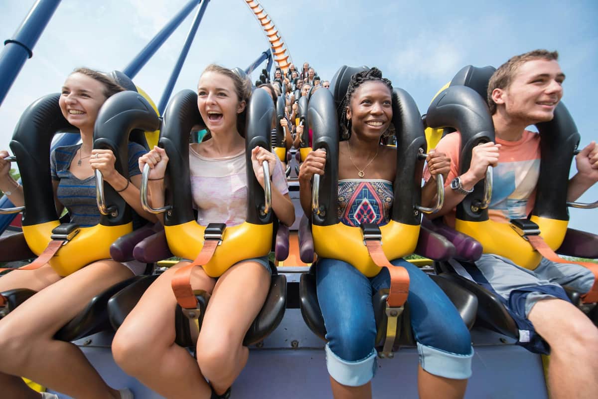 Three people, secured in roller coaster seats, smiling and enjoying the ride while the train ascends a track.