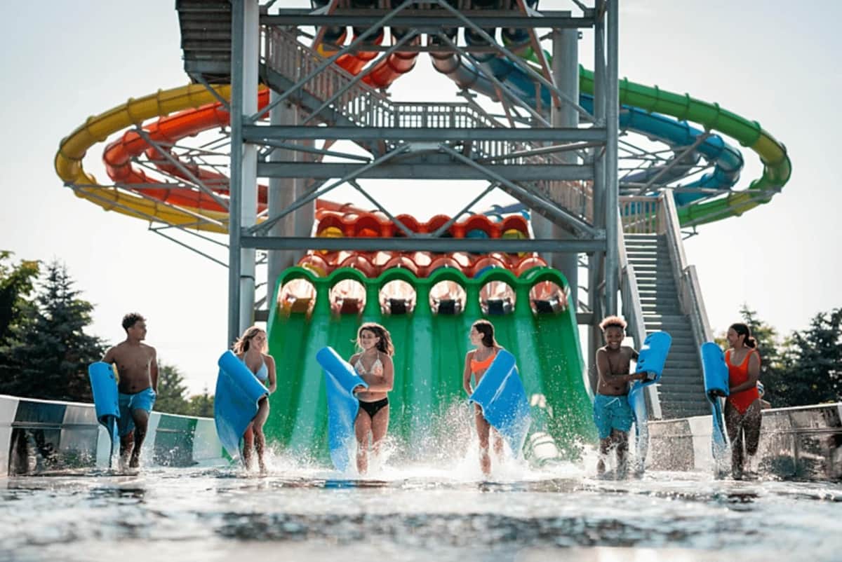 A group of people with blue mats walking in front of colorful water slides at a water park.