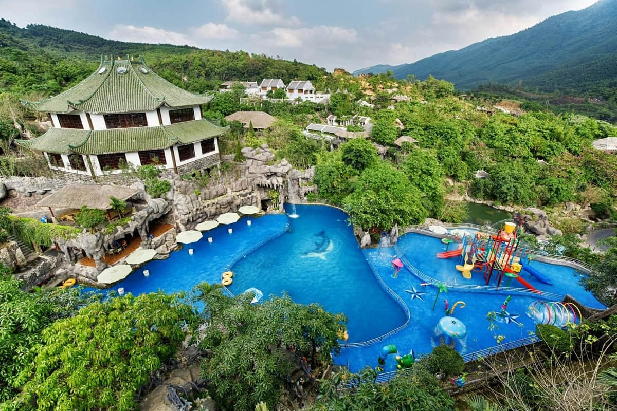 A water park with a large pool, slides, and play areas surrounded by greenery and a traditional-style building.