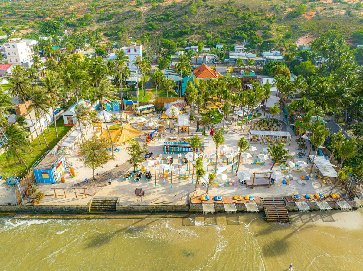 A vibrant tropical beach area with palm trees, colorful umbrellas, buildings, and people enjoying the seaside setting.