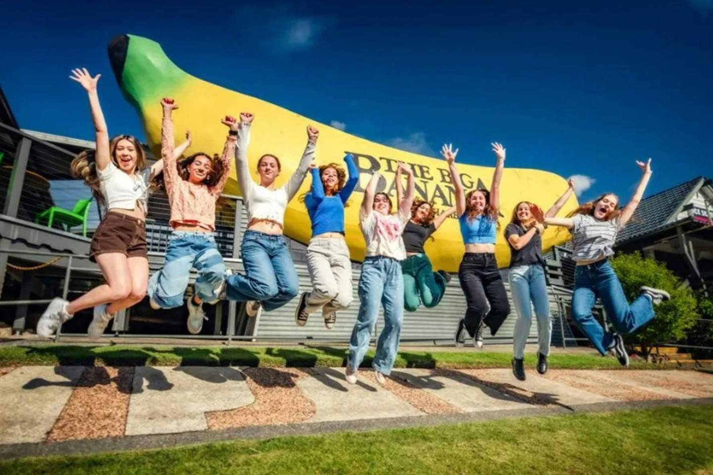 A group of people jumping in front of a large banana sculpture under a clear blue sky.