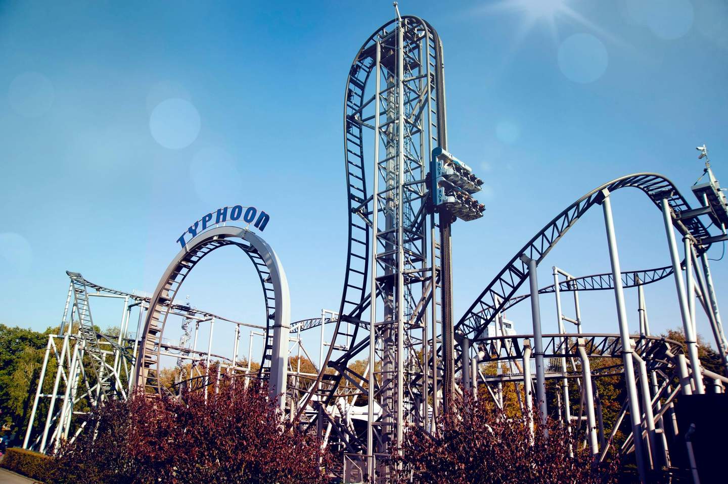 A rollercoaster named "Typhoon" with multiple loops and twists under a clear blue sky, surrounded by trees and bushes.