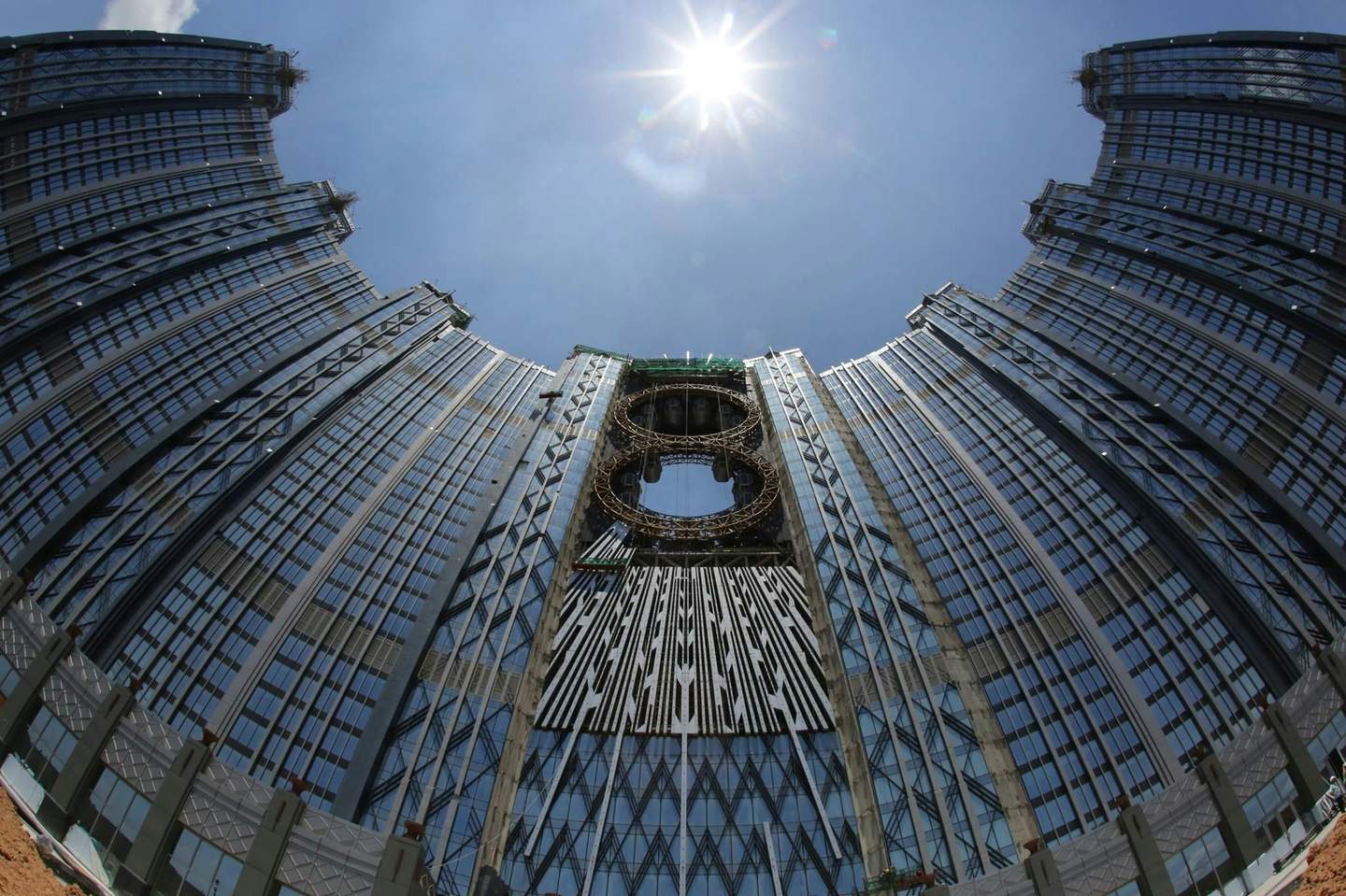 A tall, modern skyscraper with reflective glass windows towers under a bright sun in a clear blue sky.