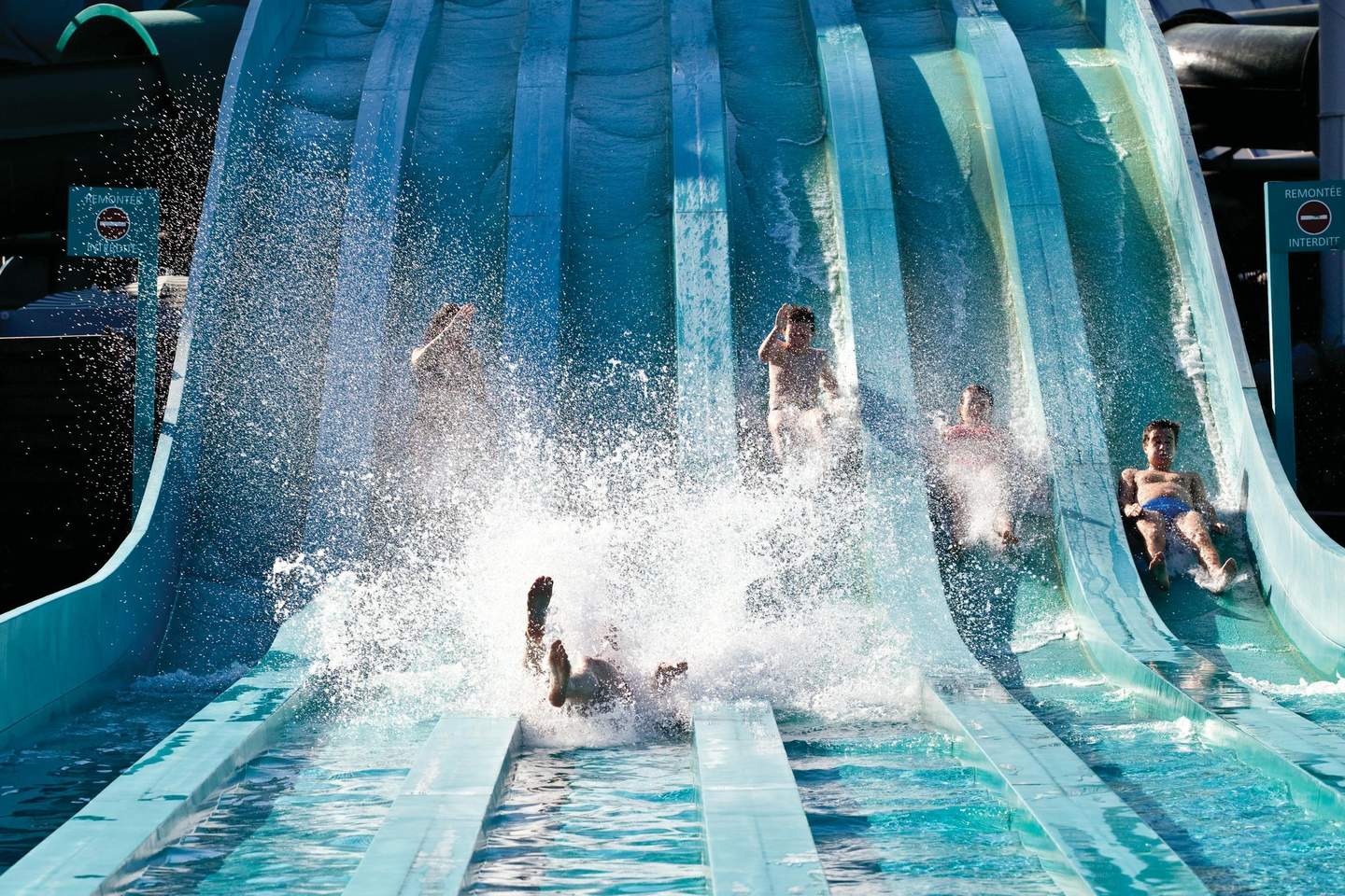 People sliding down blue water slides with splashes and a lot of water spraying around them.