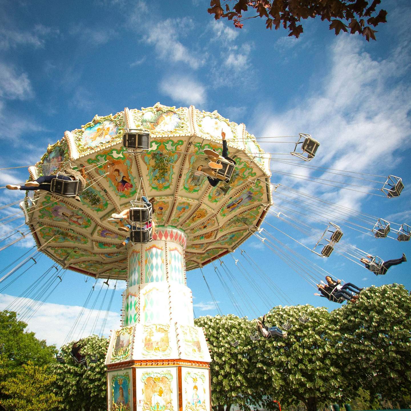 People enjoying a colorful swing ride at an amusement park, set against a blue sky with trees in the background.