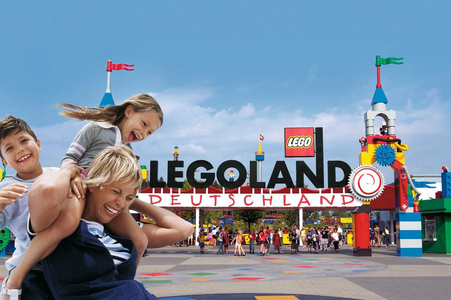 LEGOLAND® Deutschland Resort Three children laugh and play in front of the colorful entrance to LEGOLAND Deutschland under a clear blue sky.