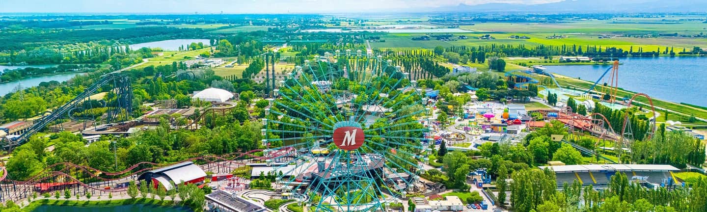 A colorful amusement park with various attractions, including a Ferris wheel, roller coasters, and surrounding greenery.