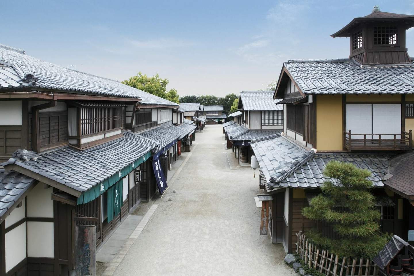 Toei Kyoto Studio Park A narrow street lined with traditional Japanese wooden buildings under a clear blue sky, with tile roofs and minimal vegetation visible.