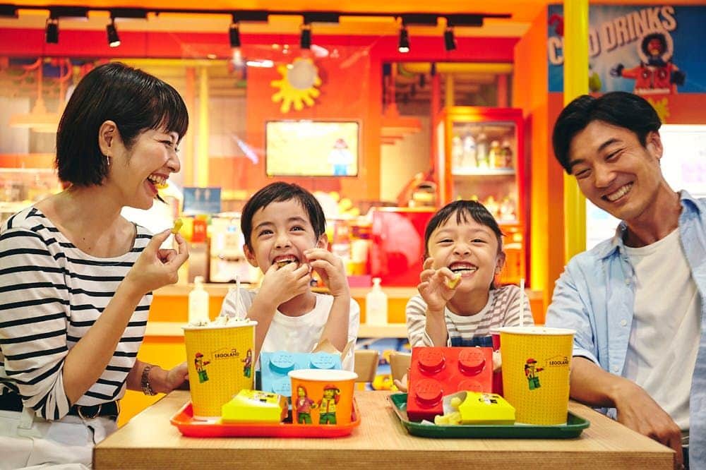 LEGOLAND Discovery Center Tokyo A family of four smiles and enjoys food at a colorful, themed restaurant with LEGO-branded cups and LEGO blocks on the trays.