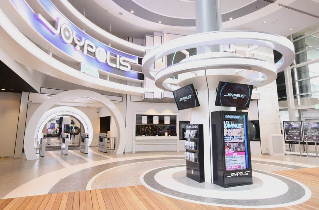 Tokyo Joypolis Modern indoor amusement park entrance with large "Joypolis" signage, electronic displays, ticket gates, and futuristic architecture.