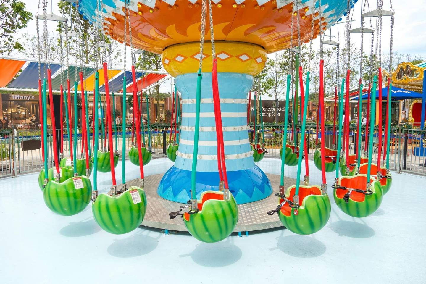 A colorful swing ride with watermelon-themed seats in an amusement park setting.