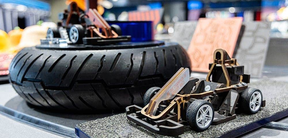 Small model race cars displayed on a textured surface with a large tire in the background.