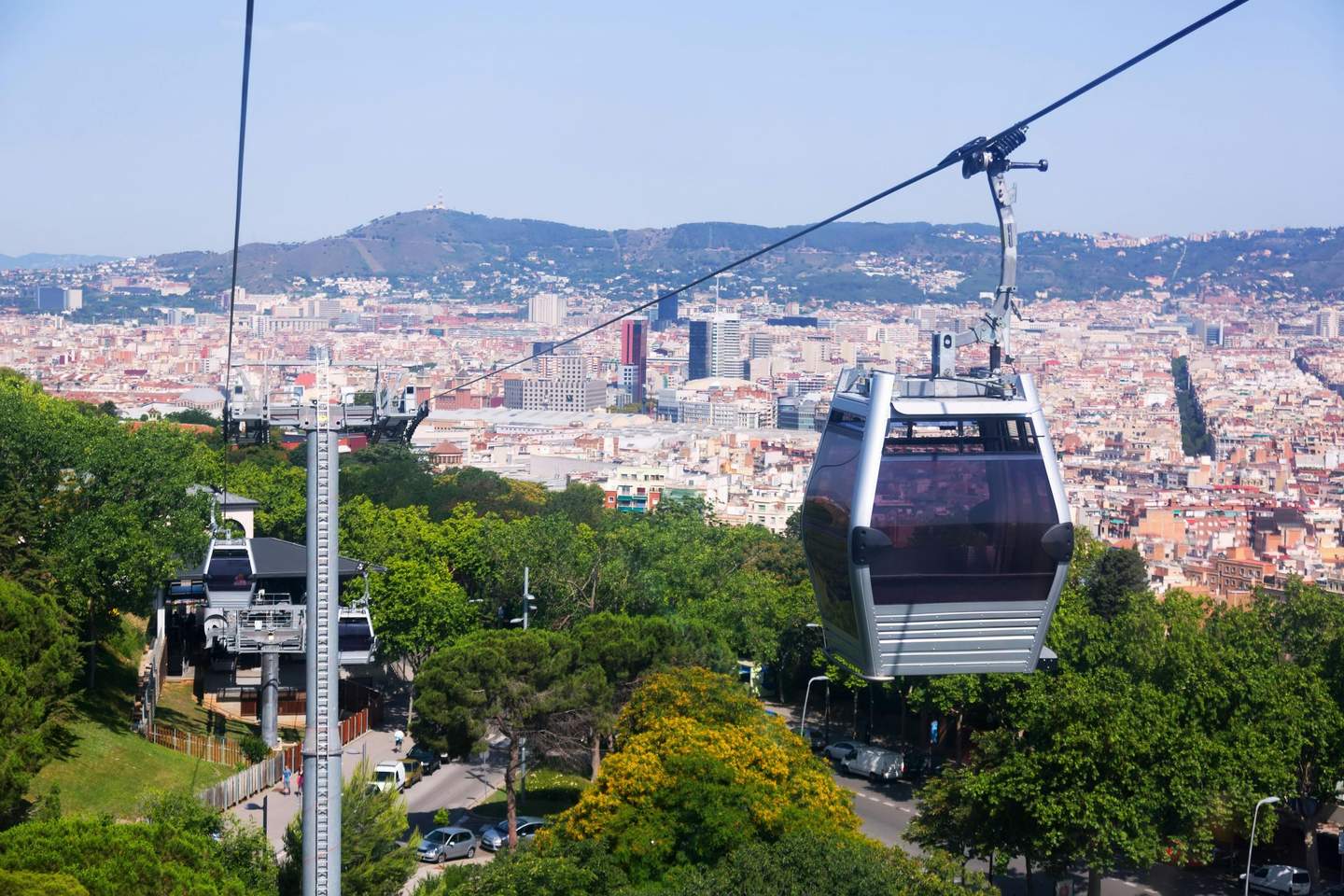 Cable cars moving above lush greenery with a densely packed cityscape and mountains in the background.