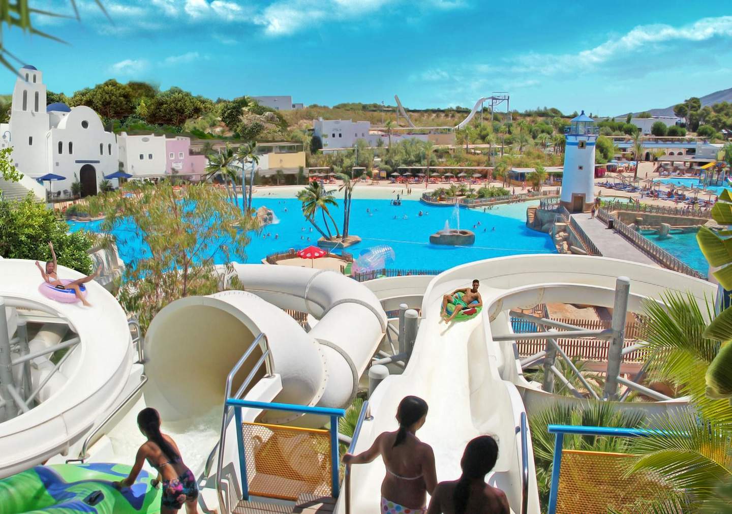 People enjoying water slides and a large pool at a water park, with buildings, trees, and a lighthouse in the background.