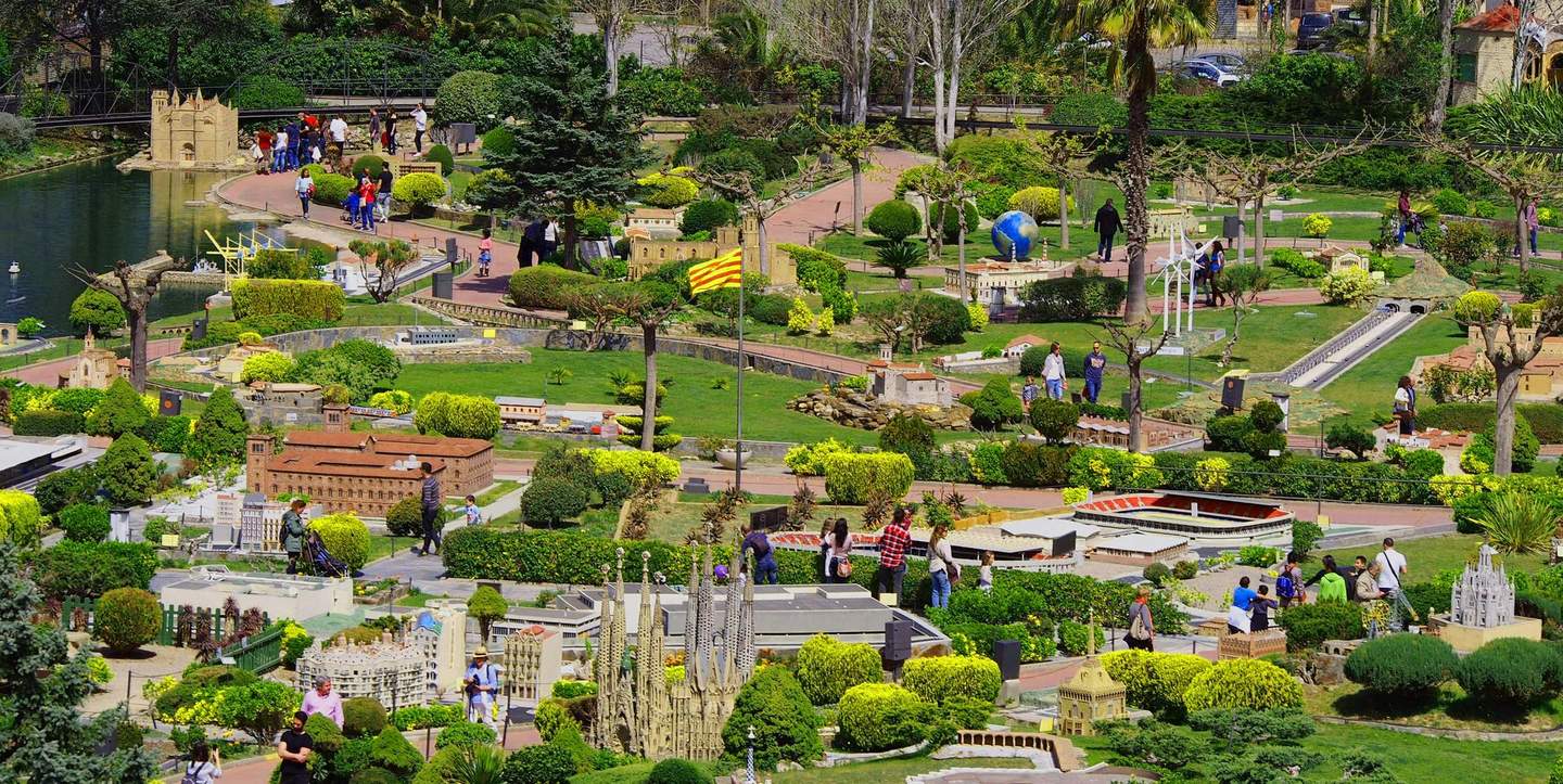 People walking through a park with miniature models of famous buildings, lush greenery, and a small pond.