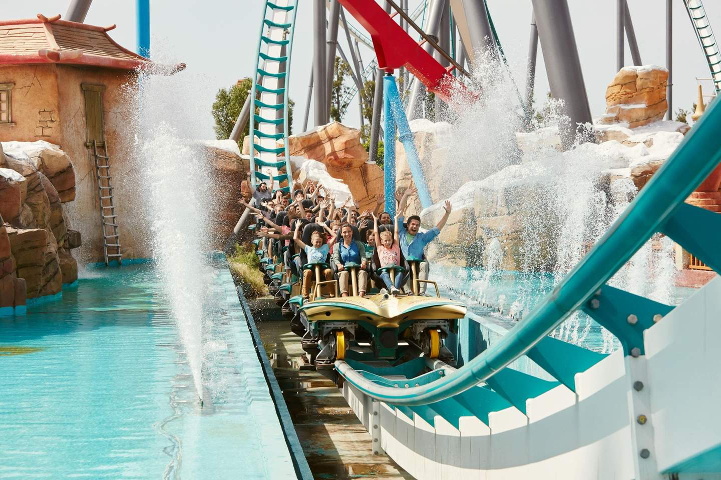 People on a water-themed rollercoaster, raising their hands and splashing through water, surrounded by rocks and structures.