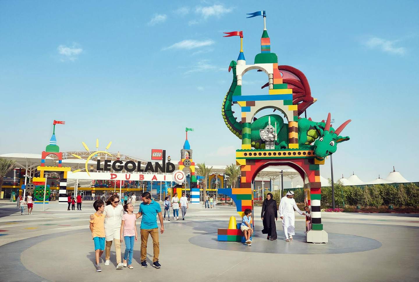 Entrance of LEGOLAND Dubai with colorful LEGO structures, people walking, and a large dragon decoration under a clear blue sky.