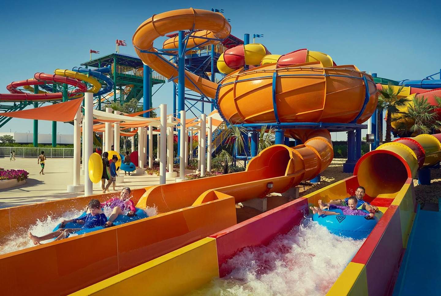 LEGOLAND® Water Park People splashing down colorful water slides on inflatable tubes at an outdoor water park under a clear blue sky.