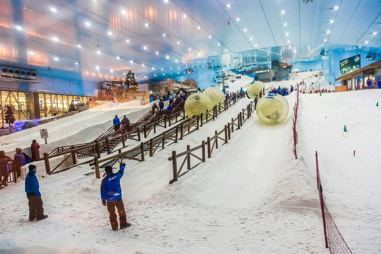 Ski Dubaï Piste de ski intérieure avec des personnes en veste bleue qui surveillent des ballons gonflables sur des rampes enneigées.